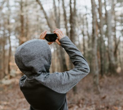 Hupparipukuinen henkilä ottaa kuvia puista metsässä.