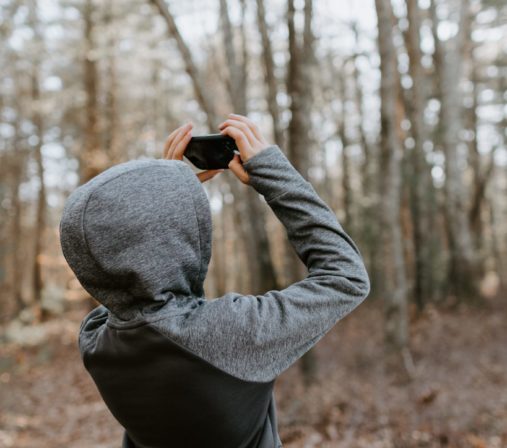 Hupparipukuinen henkilä ottaa kuvia puista metsässä.